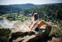 Asi desetiletá holčička v šortkách a bílém tričku sedí na velkém balvanu nad Vranovskou přehradou a dívá se směrem k ní
