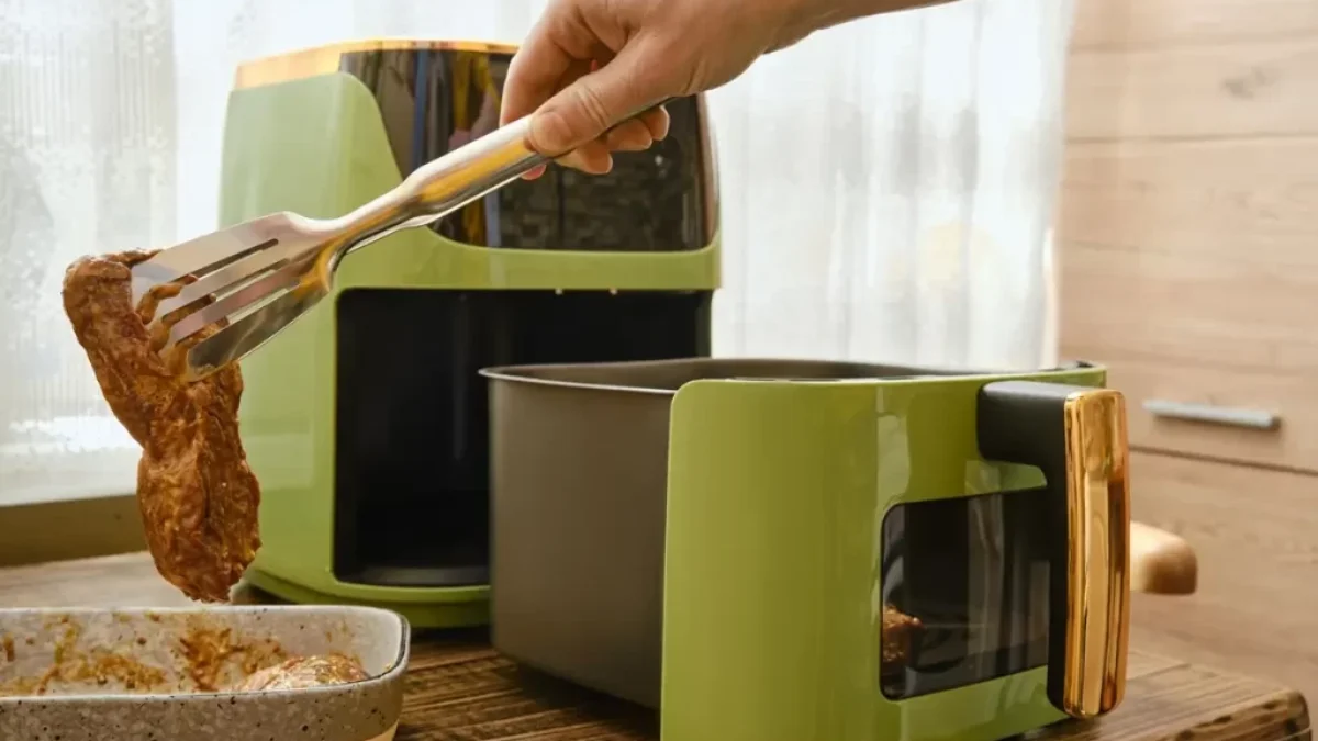 Ruka s kleštěmi, které nabírají plátek masa do horkovzdušné fritézy