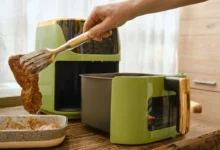 Ruka s kleštěmi, které nabírají plátek masa do horkovzdušné fritézy