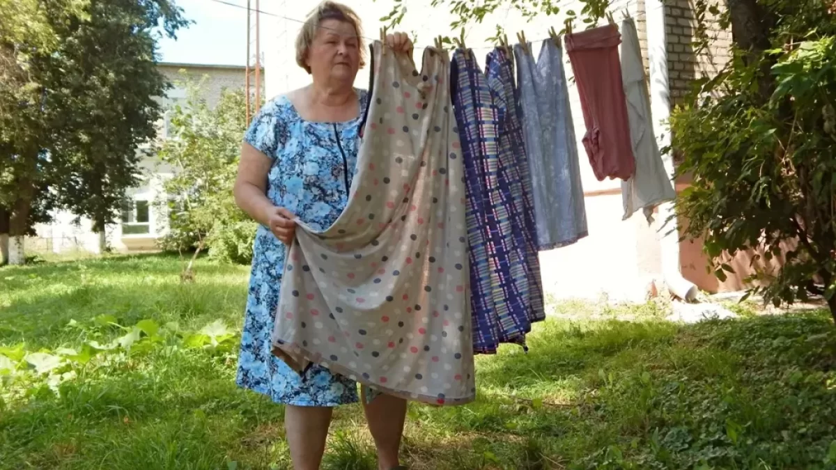 Starší žena přebírá několikatery šaty pověšené na věšáku venku
