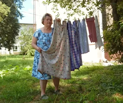 Starší žena přebírá několikatery šaty pověšené na věšáku venku