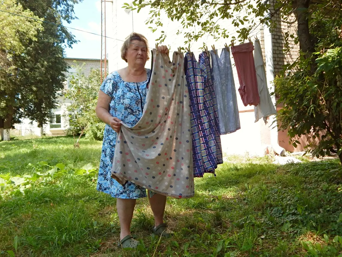 Starší žena přebírá několikatery šaty pověšené na věšáku venku