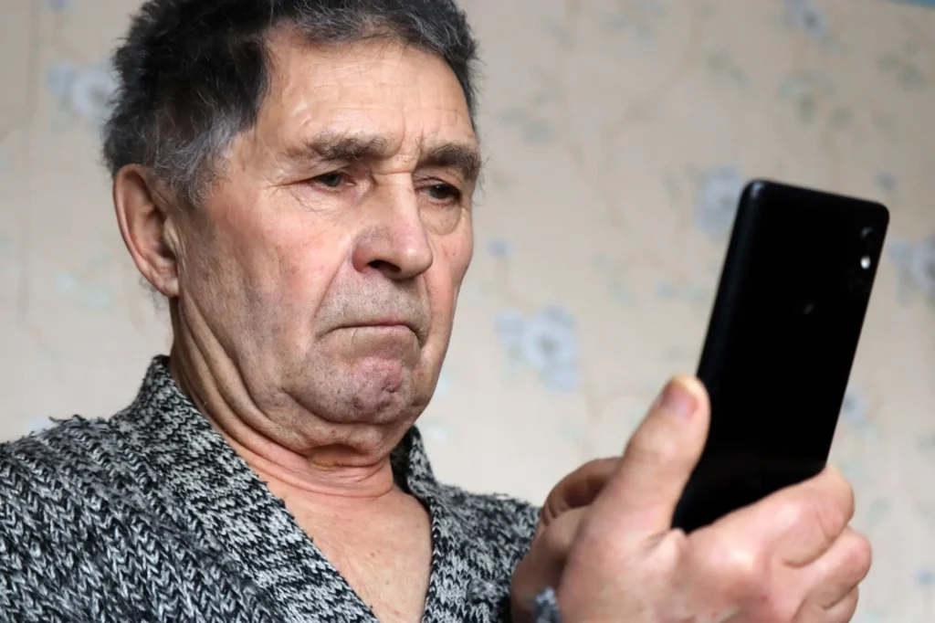 senior se mračí na displej telefonu