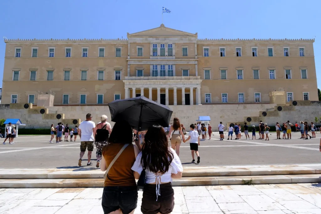 Turisté cestující po Evropě by si měli dát pozor na vysoké teploty. - SportDeník turisté chránící se deštníkem před sluncem