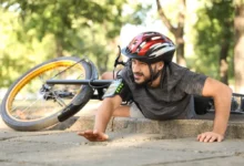 Mladý muž ve sportovním oděvu leží na zemi vedle svého kola po pádu