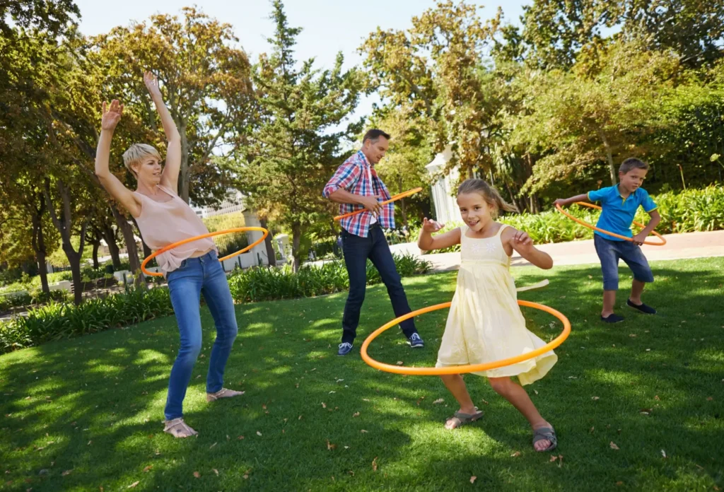 - SportDeník Děti i dospělí společně cvičí s hula hoop obručemi venku na zahradě.