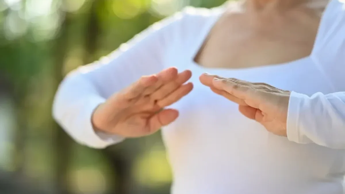 Starší žena v bílém tričku cvičí tai-chi