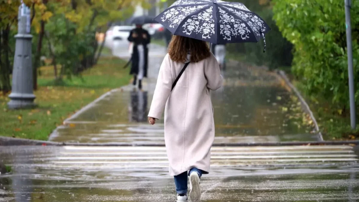 Žena v dlouhém svetru jde s deštníkem podzimním parkem