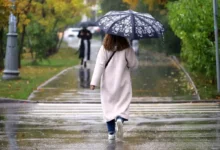 Žena v dlouhém svetru jde s deštníkem podzimním parkem