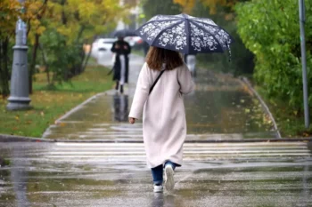 Žena v dlouhém svetru jde s deštníkem podzimním parkem