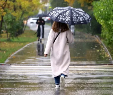 Žena v dlouhém svetru jde s deštníkem podzimním parkem