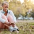 Starší žena v seniorském věku sedí v podzimní přírodě na zemi a směje se