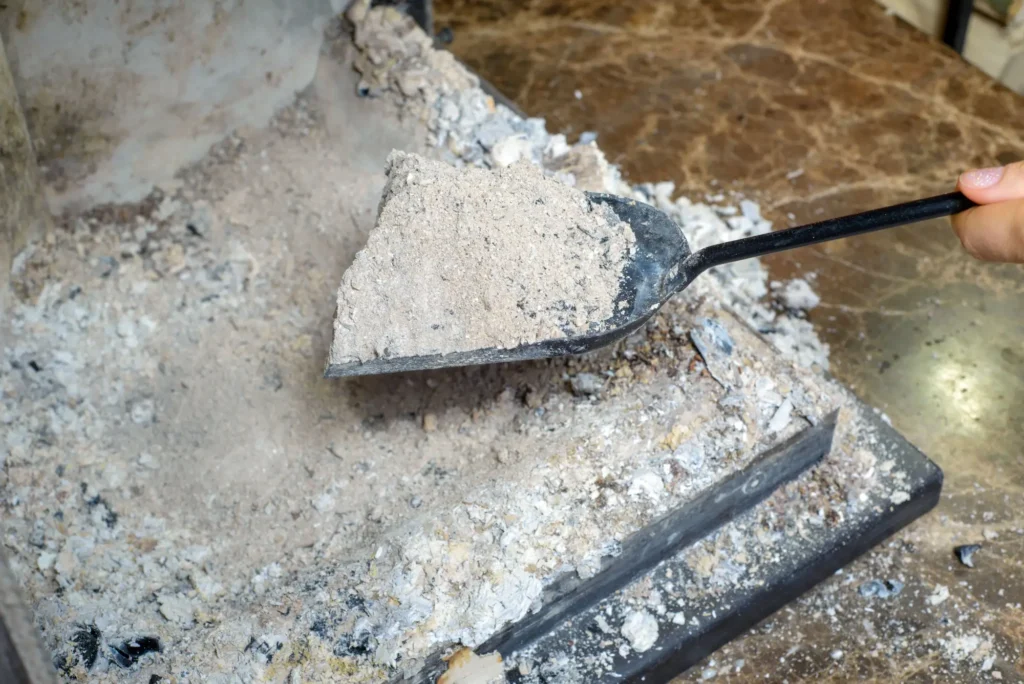 Ruka nabírá popel z krbu na lopatku
