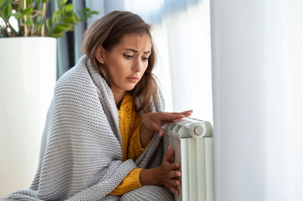 Maldá žena sedí přikrytá dekou u radiátoru