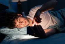 Mladý muž ležící v posteli a koukající do telefonu