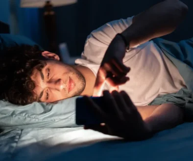 Mladý muž ležící v posteli a koukající do telefonu