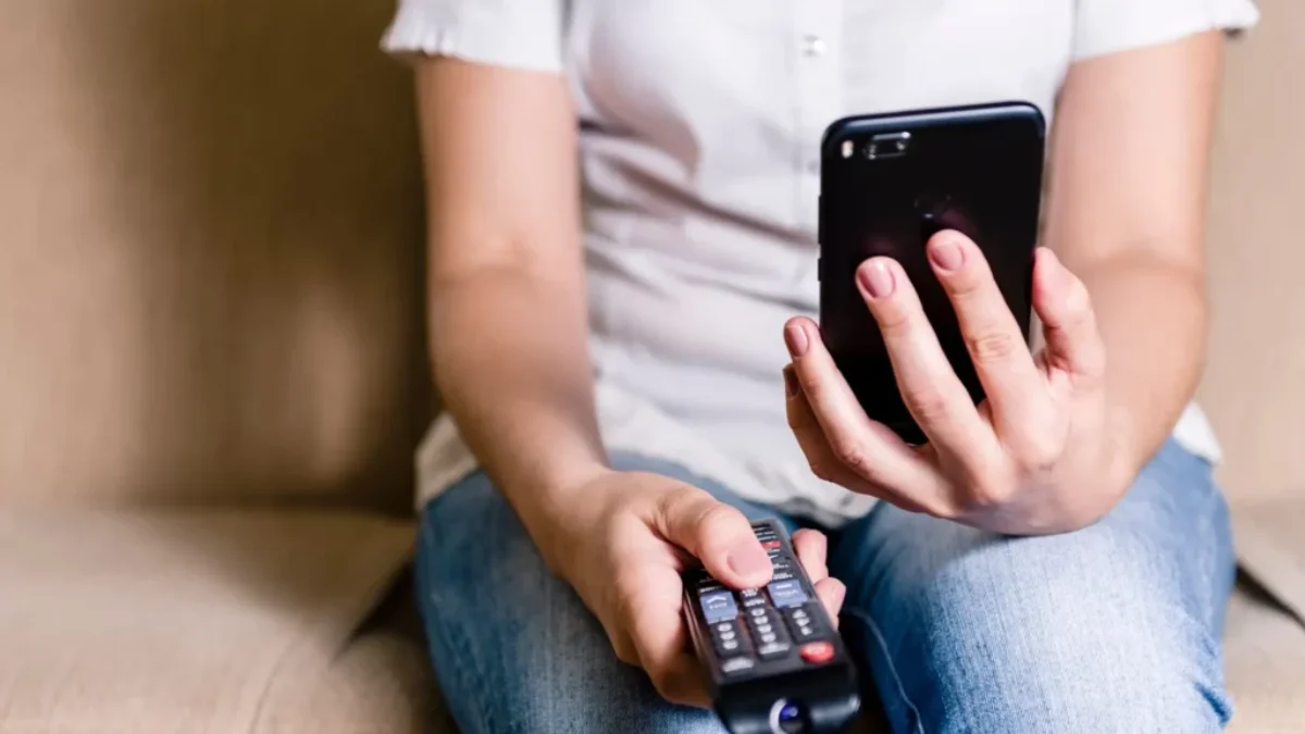 žena s ovladačem od televize a mobilem