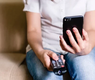 žena s ovladačem od televize a mobilem