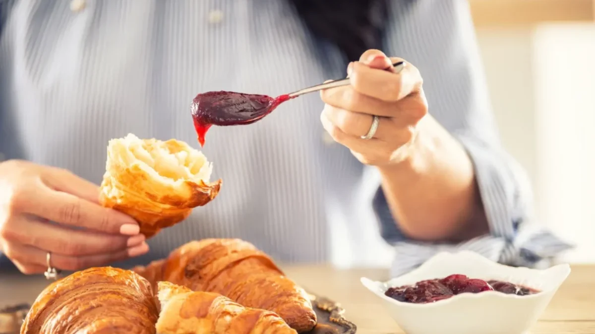žena si na croissant dává marmeládu