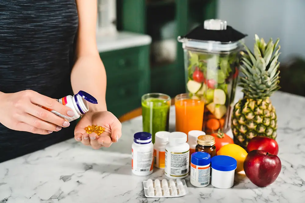 Veškeré vitaminy lze získat přirozeným způsobem. Zdroj: Shutterstock - SportDeník žena si přpravuje smoothie a k tomu bere vitamíny