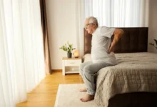 senior vstává z postele a drží se záda