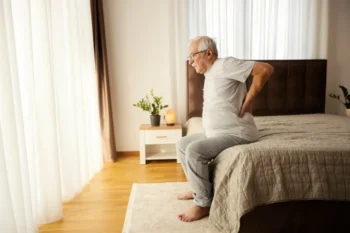 senior vstává z postele a drží se záda