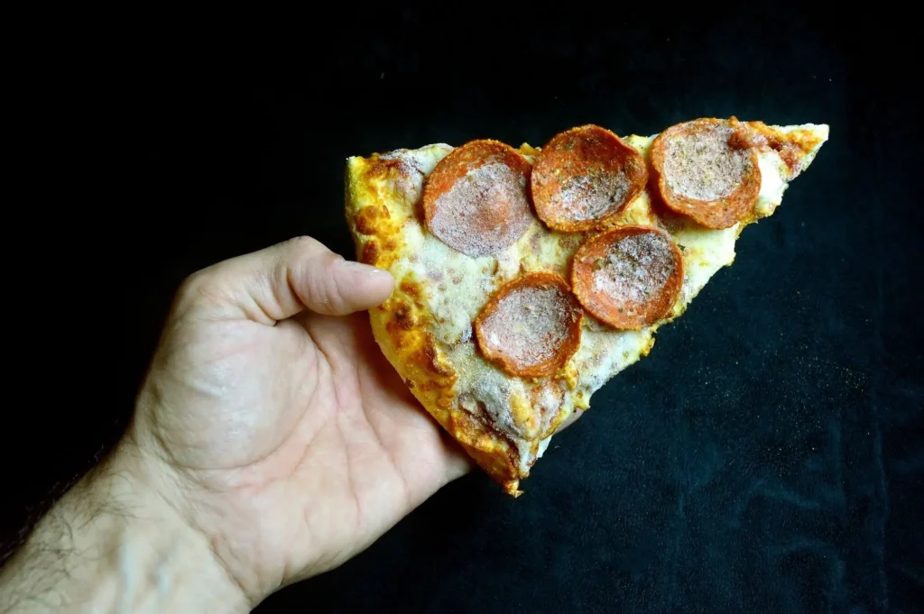 shutterstock_755015062 - SportDeník detail na mužskou ruku s jedním plátkem mražené pizzy