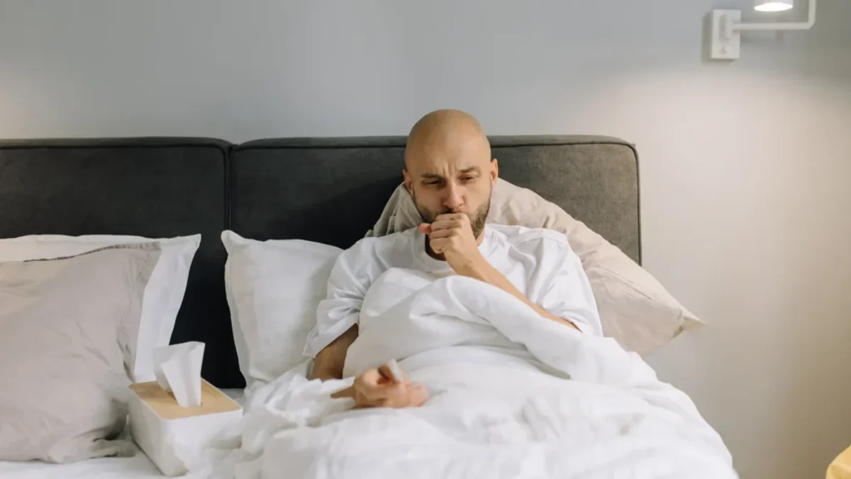 muž leží v posteli s kašlem