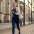 Woman jogging along a tree-lined cobblestone street with historic stone buildings in the background, smiling.