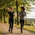 Two women in athletic wear jogging along a tree-lined trail with a river valley in the background.
